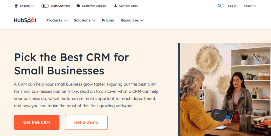 Two women interact at a counter in a business setting, with a HubSpot CRM promotion and call-to-action buttons on the website.