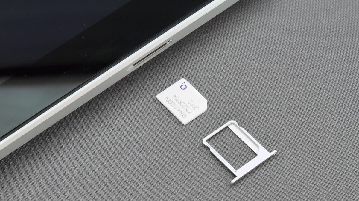 A SIM card and SIM tray are placed next to a tablet device on a gray surface.