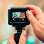Close-up of hands holding a camera, capturing a busy city street scene visible on the camera’s display screen.