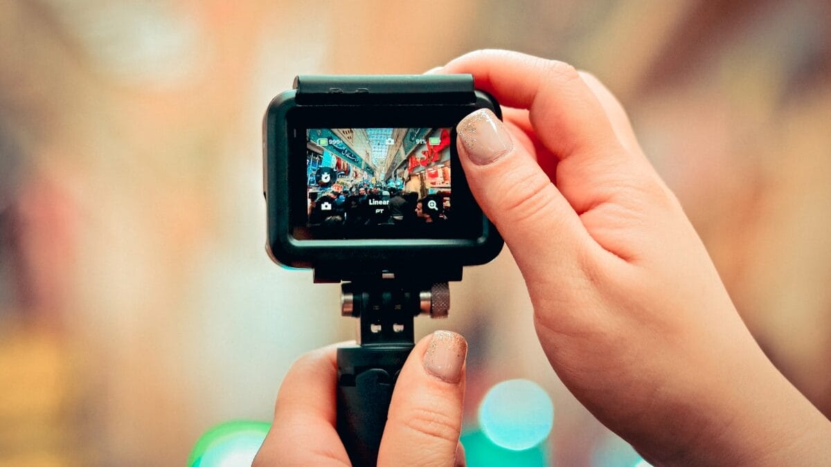 Close-up of hands holding a camera, capturing a busy city street scene visible on the camera’s display screen.