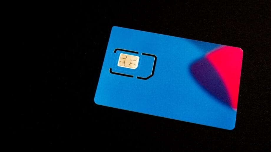 A blue SIM card with a visible chip rests on a black surface, partially illuminated by red and blue light.