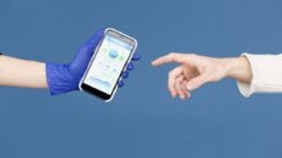 A gloved hand holds a smartphone displaying a health app as an ungloved hand reaches toward it, against a blue background.