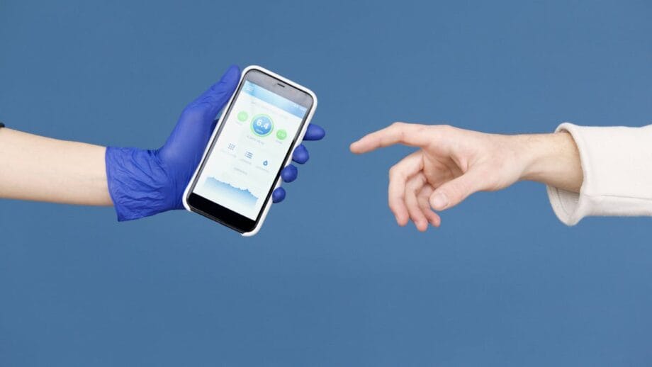 A gloved hand holds a smartphone displaying a health app as an ungloved hand reaches toward it, against a blue background.