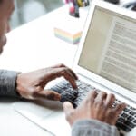 A person types on a laptop keyboard with a document open on the screen at a desk.