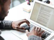 A person types on a laptop keyboard with a document open on the screen at a desk.