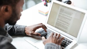 A person types on a laptop keyboard with a document open on the screen at a desk.