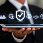 A person in a suit holds a tablet displaying floating digital icons representing security, logistics, and business processes.