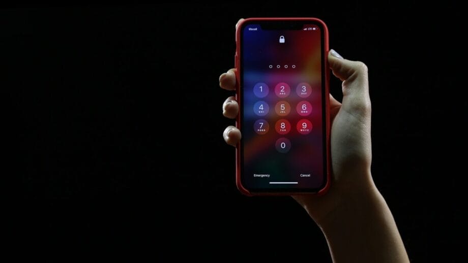 A hand holds a smartphone displaying a passcode entry screen against a black background.