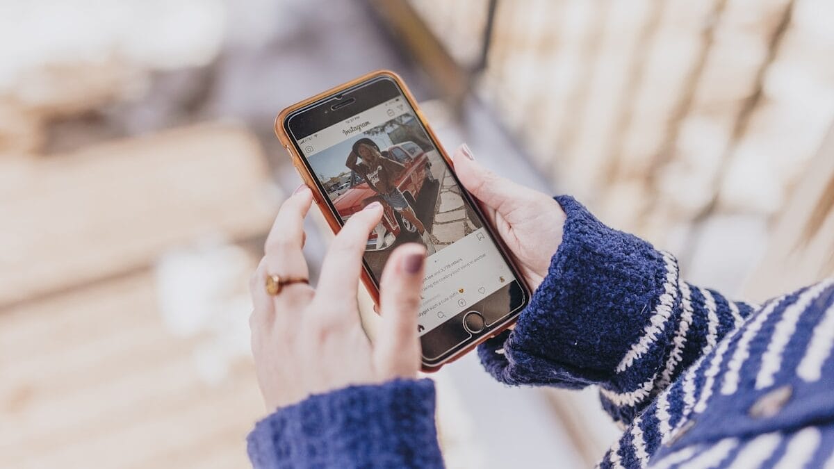 Person in a blue sweater holding a smartphone and viewing a short-form video of a woman on Instagram outdoors.