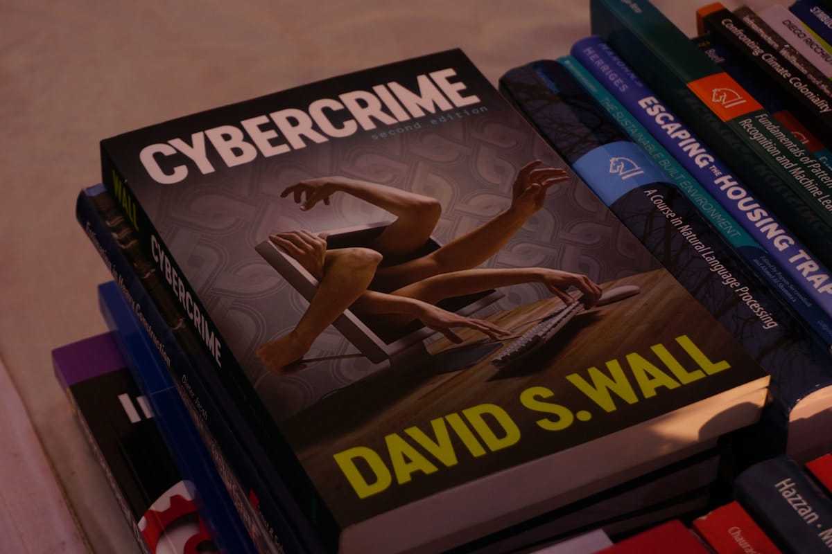A stack of books with Cybercrime by David S. Wall on top, featuring an abstract cover with arms emerging from a laptop.