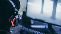Person wearing illuminated gaming headset playing a video game on a computer with a lit keyboard.