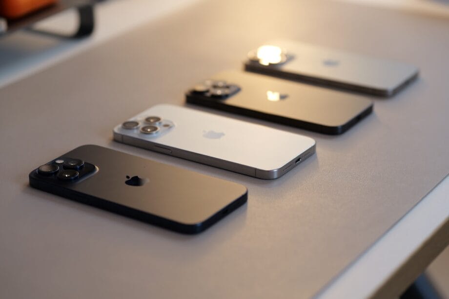 Four iPhones in different colors are placed face down in a row on a gray surface.