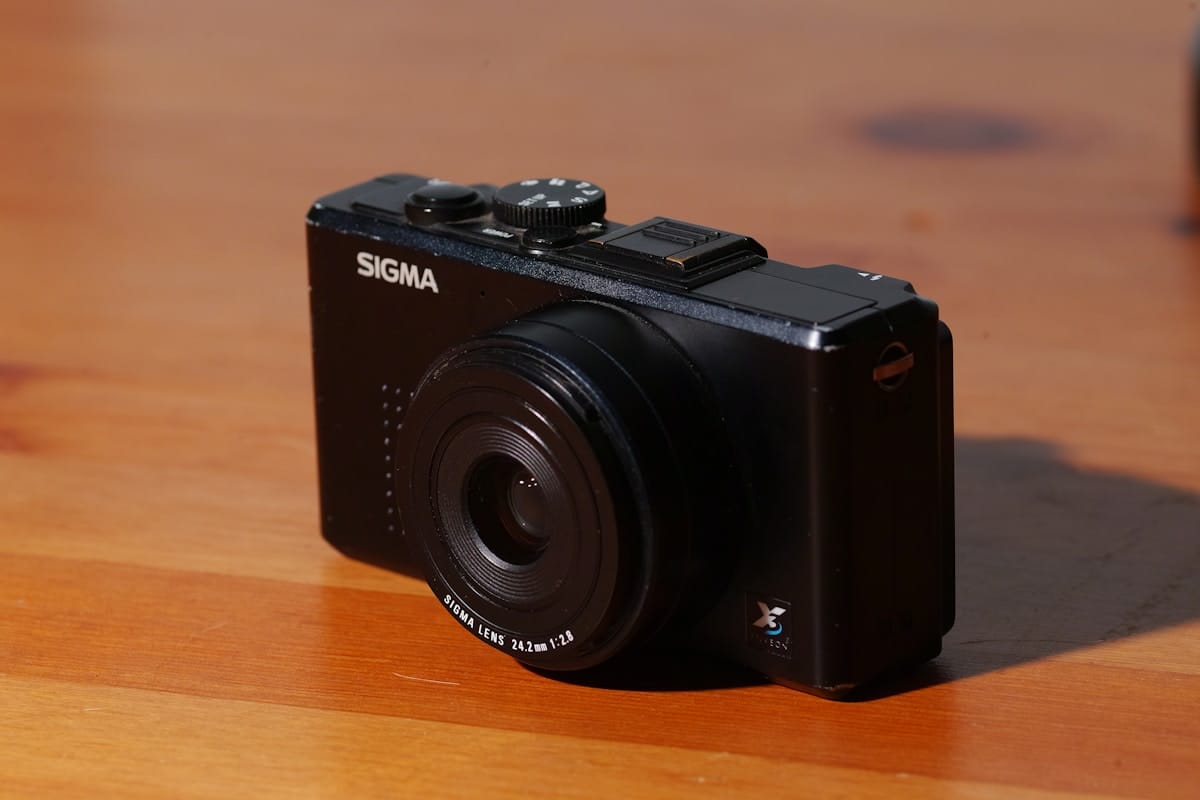 A black Sigma digital camera rests on a wooden surface in natural light.