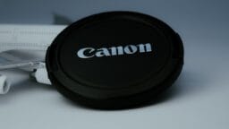 A black Canon camera lens cap resting on a surface with part of a white model airplane visible in the background.
