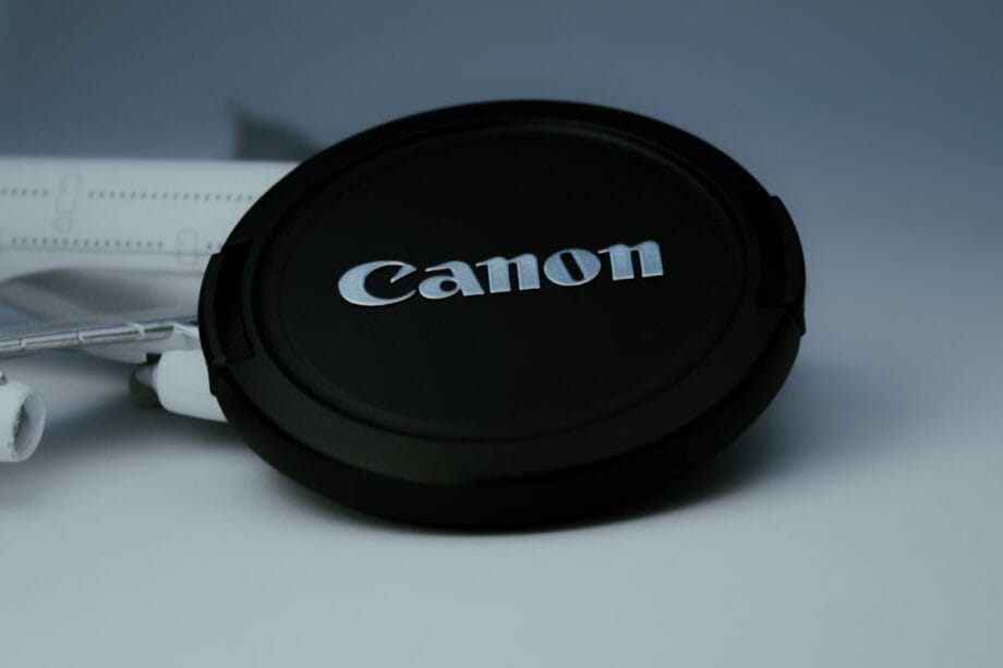 A black Canon camera lens cap resting on a surface with part of a white model airplane visible in the background.
