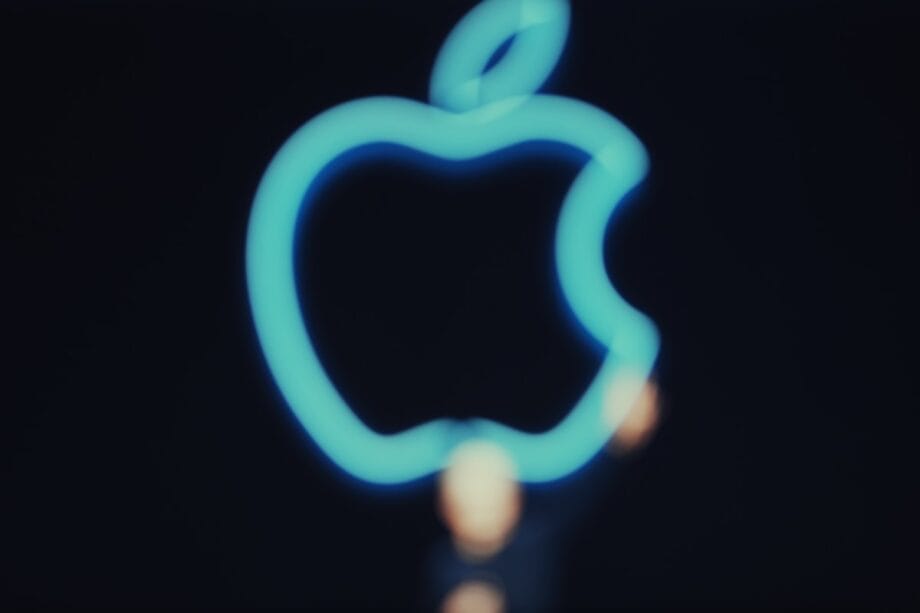 A glowing blue outline of the Apple logo against a dark background, with the image slightly out of focus.