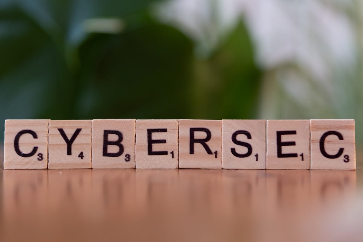 Wooden Scrabble tiles on a table spell out CYBERSEC with a blurred green background.