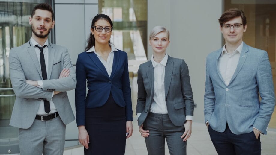 Four business professionals standing together indoors.