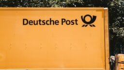 Side view of a yellow Deutsche Post delivery truck with company logo and trees in the background.