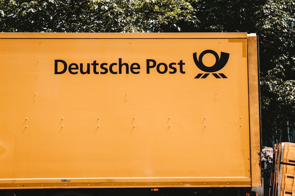 Side view of a yellow Deutsche Post delivery truck with company logo and trees in the background.