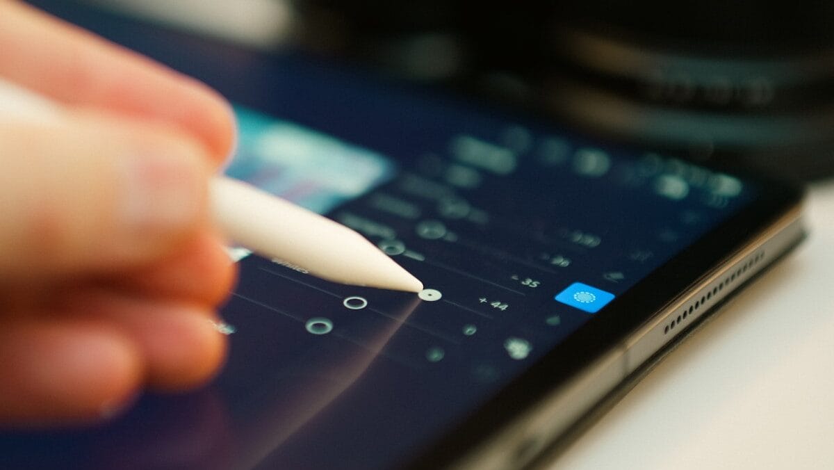 Close-up of a hand using a stylus to adjust settings on a tablet screen displaying a digital interface.