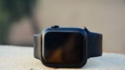 A black smartwatch with a blank screen and silicone band is placed on a light-colored surface.