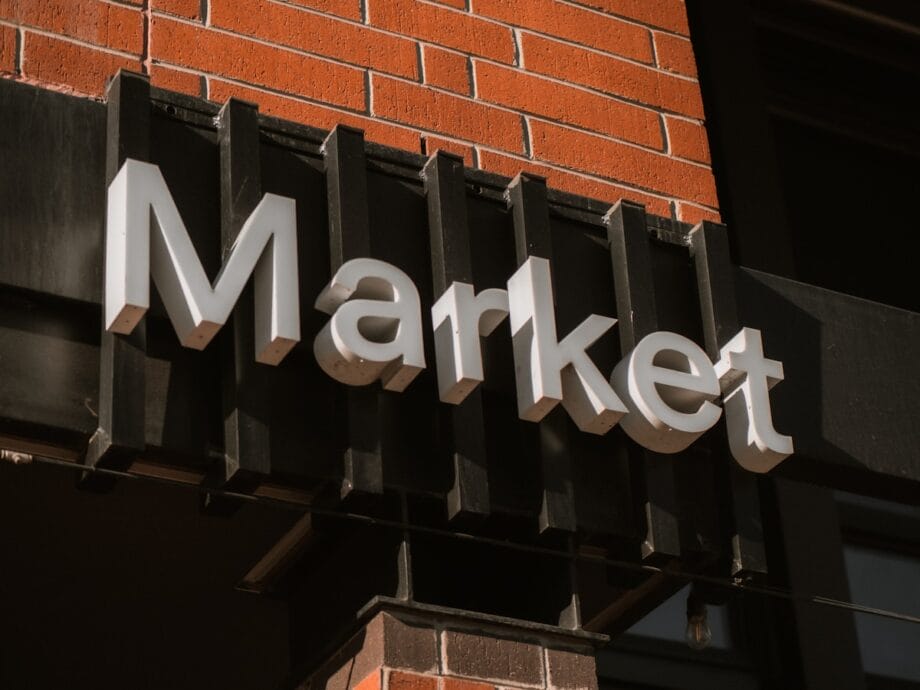 A sign reading Market is mounted on a black fixture attached to a brick wall.