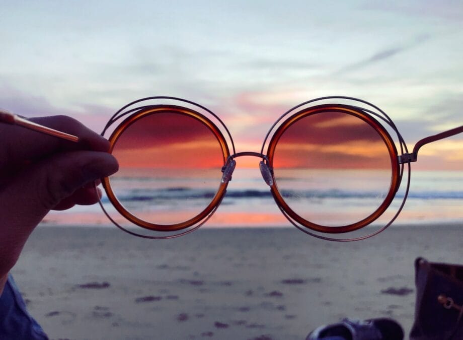 a person holding up a pair of sunglasses on the beach