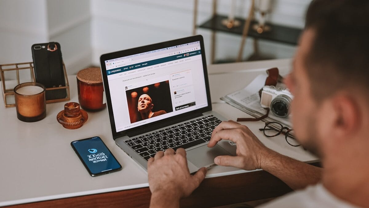 A person uses a laptop at a desk with a camera, notebook, and phone displaying Online Marketing nearby.