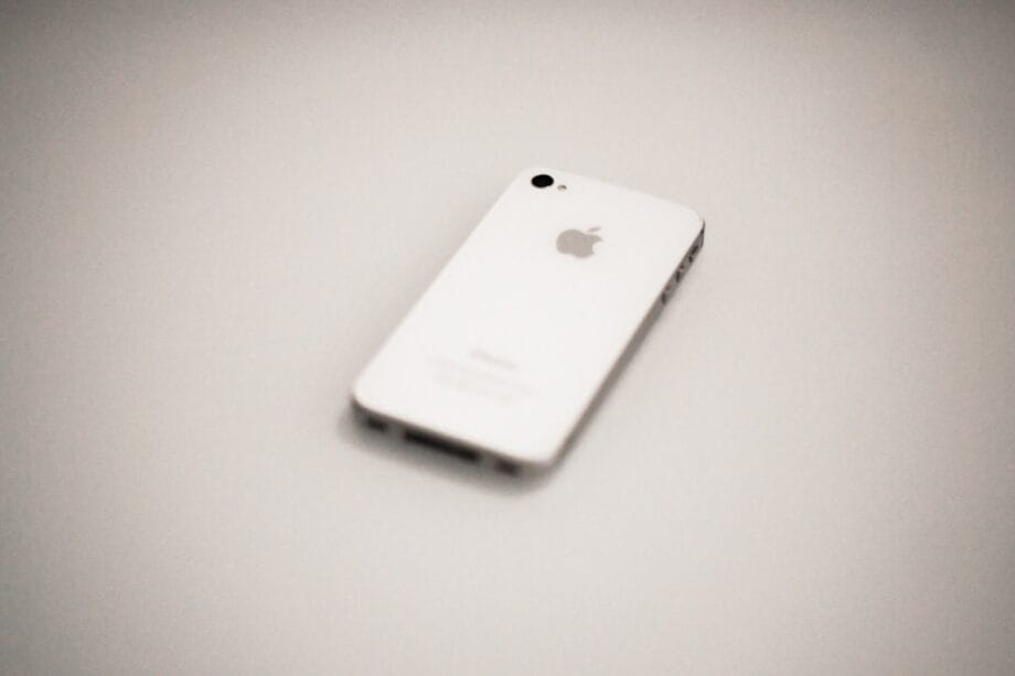 A white iPhone is lying face down on a plain, light-colored surface.