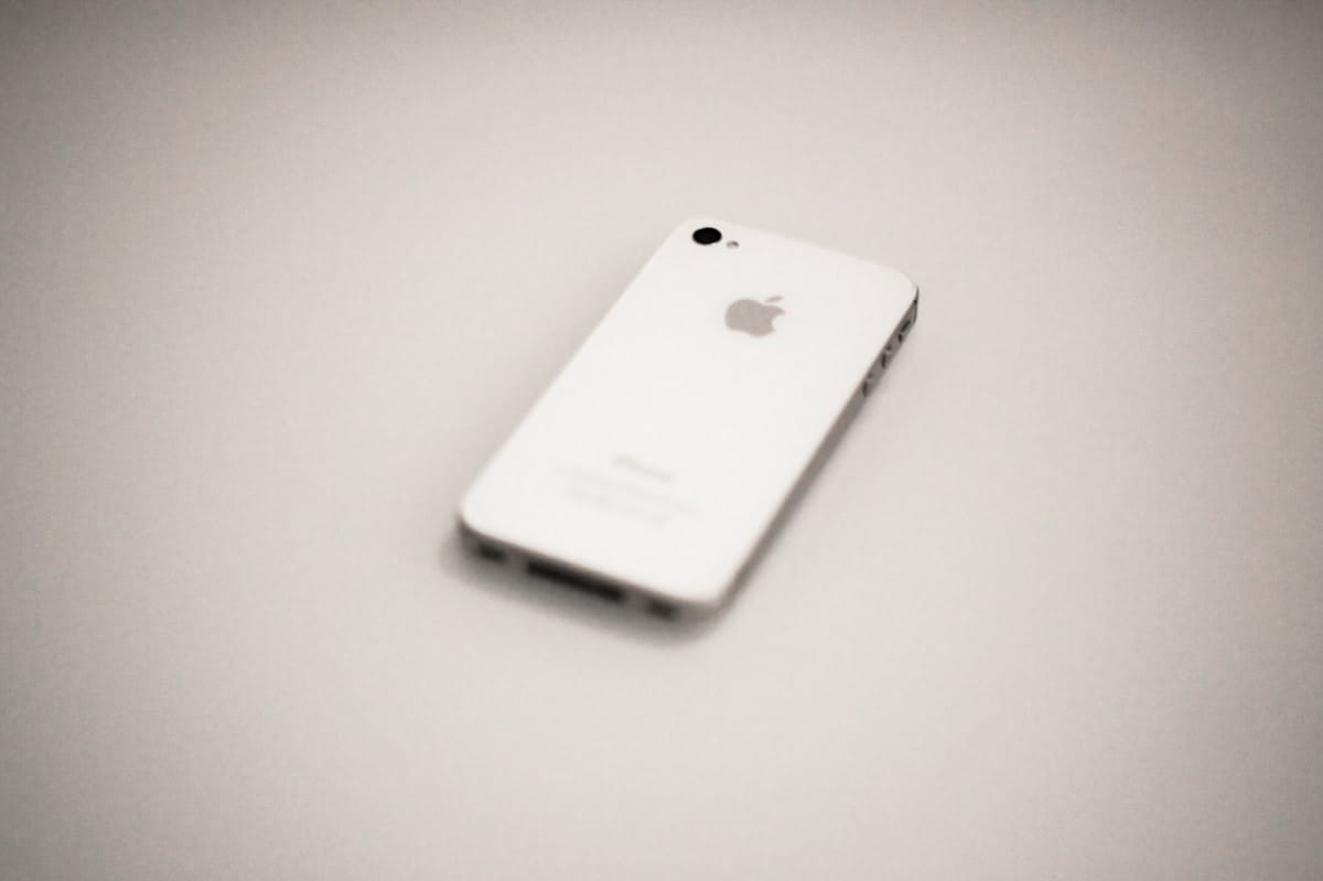 A white iPhone is lying face down on a plain, light-colored surface.