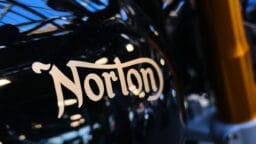 Close-up of a black motorcycle fuel tank with the word Norton in beige lettering.