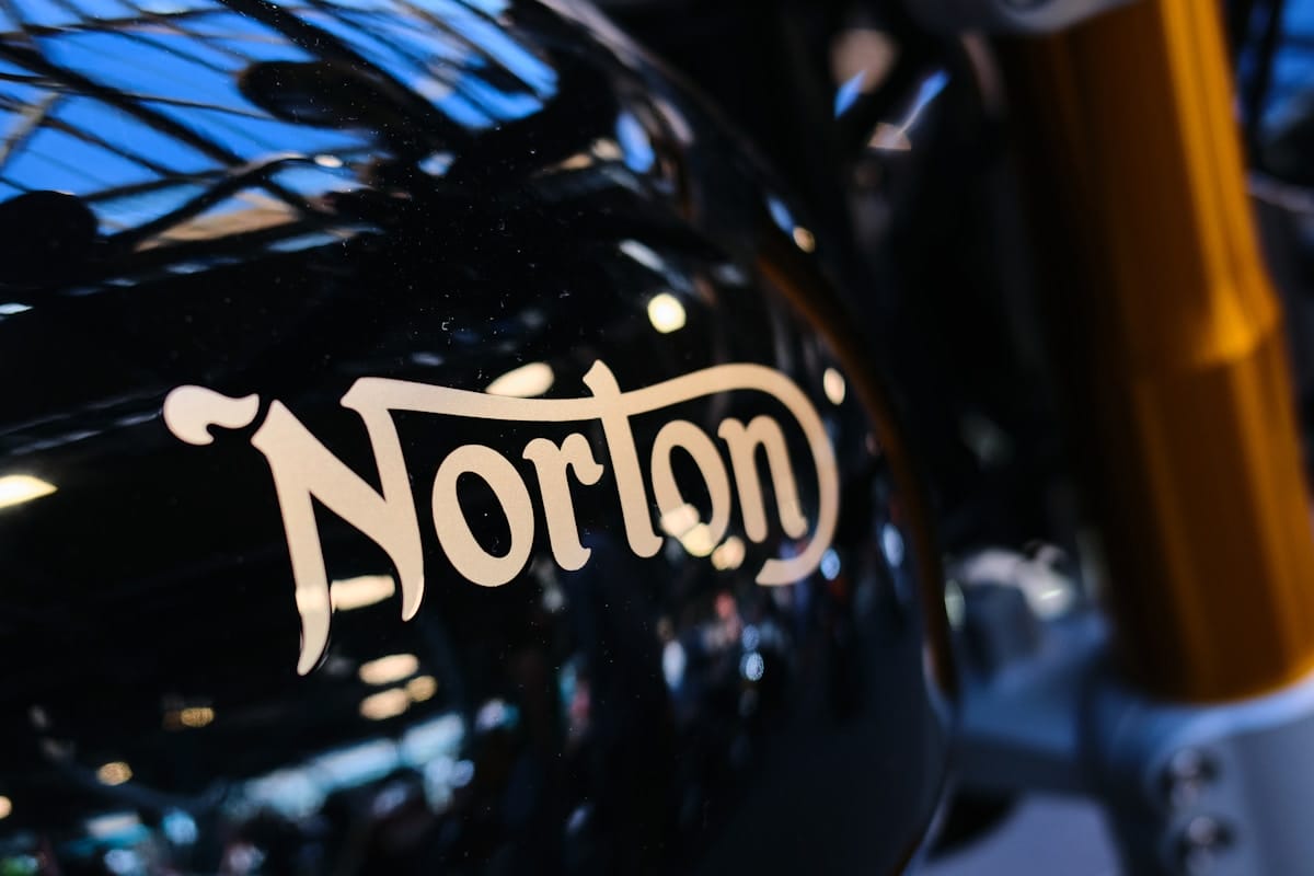 Close-up of a black motorcycle fuel tank with the word Norton in beige lettering.