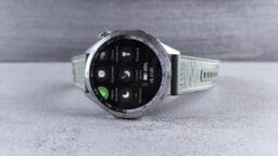 A silver smartwatch with a light gray strap displaying various health and sleep tracking icons on its screen, placed on a gray surface.