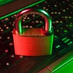A brass padlock sits on a laptop keyboard illuminated by red and green lights, symbolizing cybersecurity or data protection.