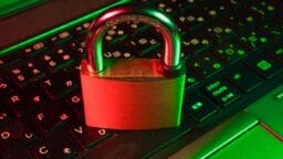 A brass padlock sits on a laptop keyboard illuminated by red and green lights, symbolizing cybersecurity or data protection.