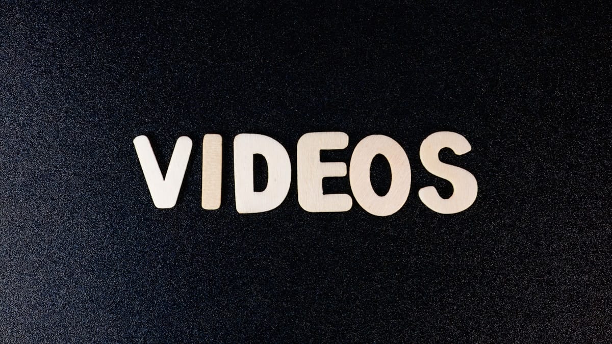 Wooden letters spelling VIDEOS are arranged on a black textured background.