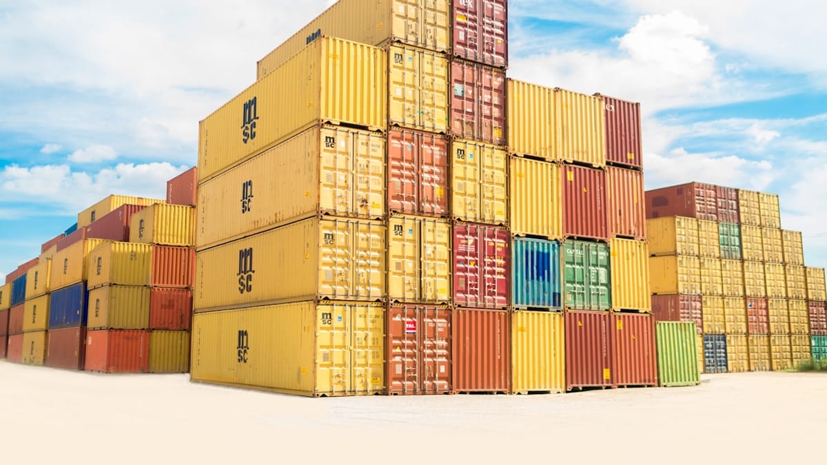 Stacks of colorful shipping containers are arranged outdoors under a partly cloudy sky.