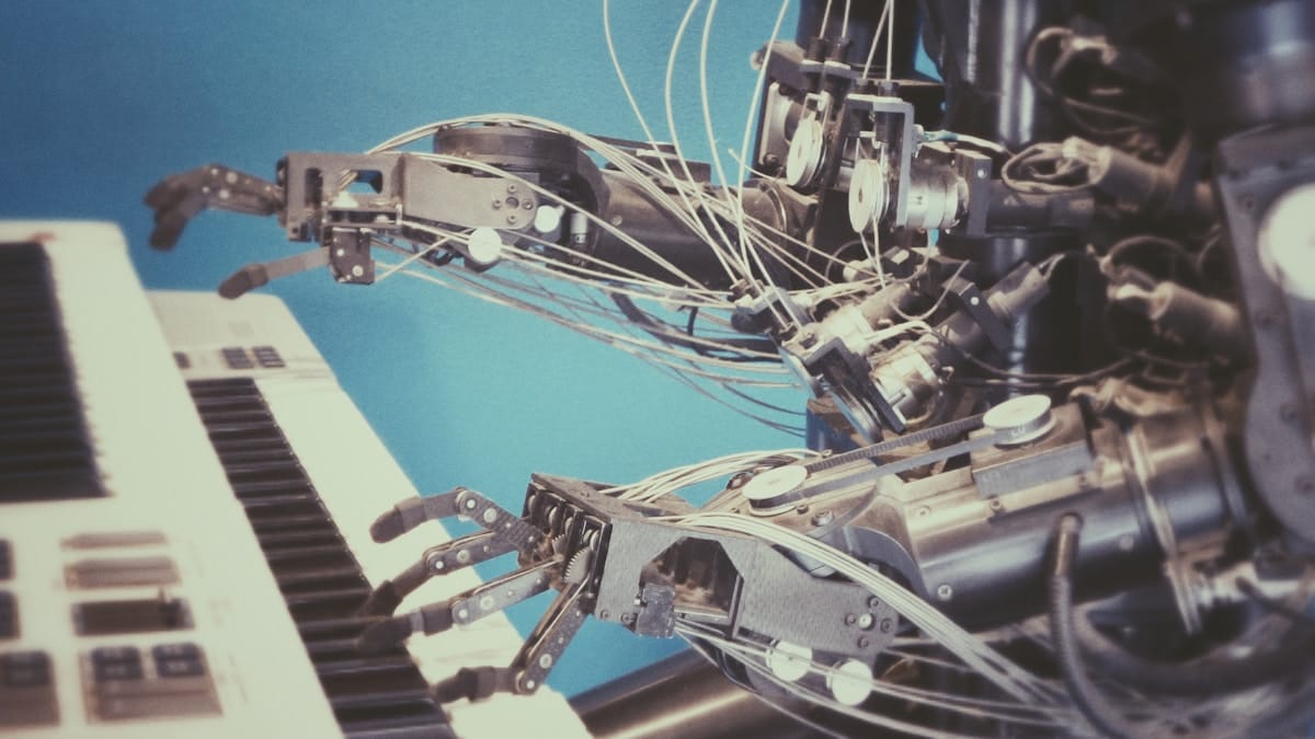 Robotic hands with wires play a keyboard synthesizer against a blue background.
