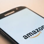 A smartphone displays the Amazon logo on its screen, with the top edge of the phone labeled Samsung.