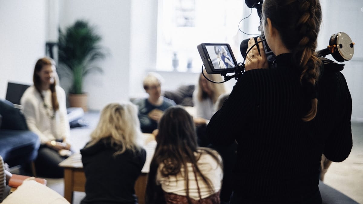 A person films a group of people sitting and talking in a casual indoor setting.