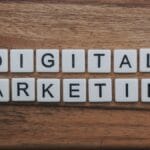 Letter tiles arranged on a wooden surface spell out Digital Marketing in two rows.