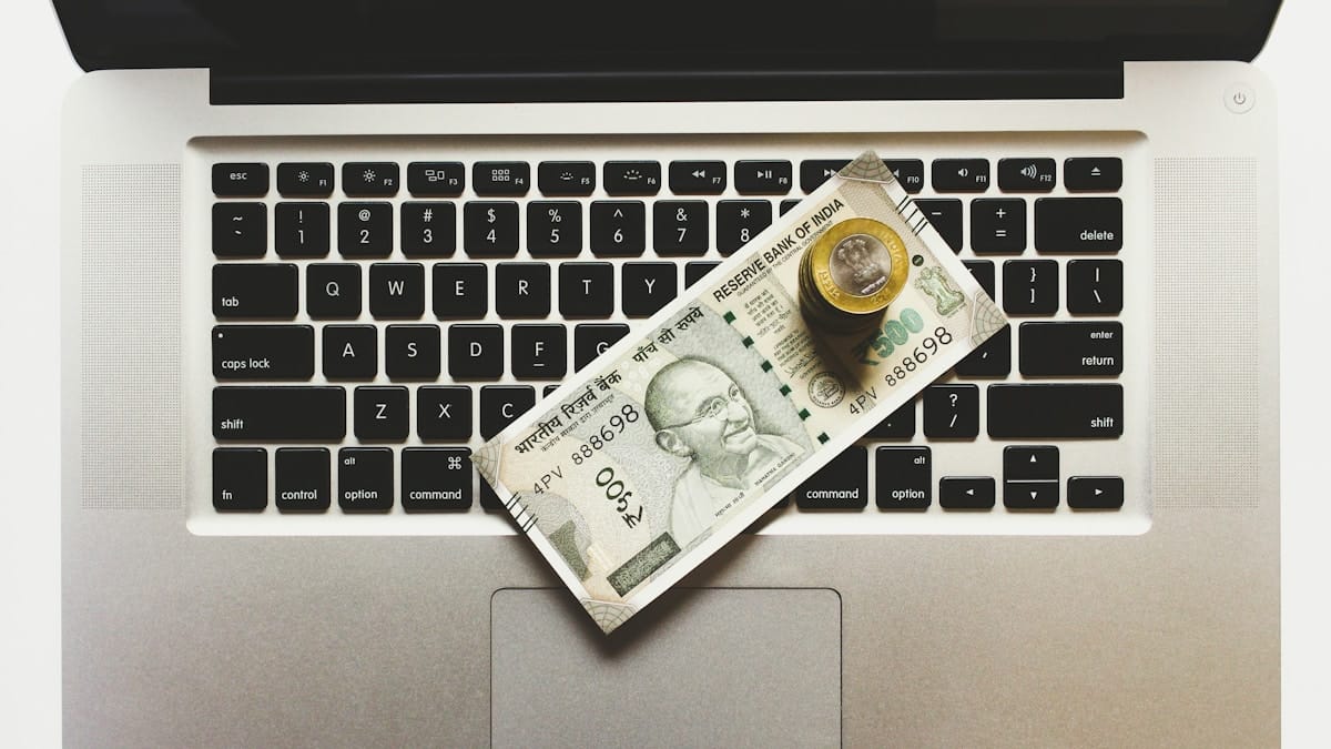 A 500 Indian rupee note and coins placed on a laptop keyboard.