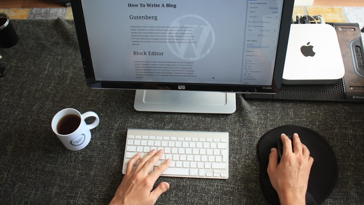 Person using a computer to write a blog post, with a cup of coffee and a Mac Mini on the desk.
