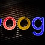 Neon Google logo sign in blue, red, yellow, and green letters on a dark, textured background.