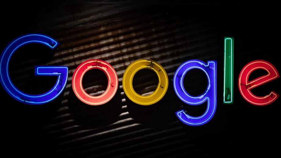 Neon Google logo sign in blue, red, yellow, and green letters on a dark, textured background.