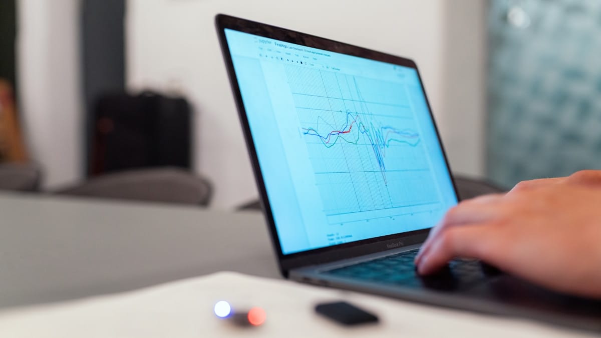 A person uses a laptop displaying a line graph with multiple data lines in a modern office setting.