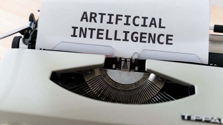 A typewriter with a sheet of paper displaying the text ARTIFICIAL INTELLIGENCE in bold uppercase letters.