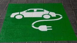 White electric car and charging plug symbol painted on a green square, indicating an electric vehicle charging station.