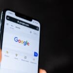 A hand holds a smartphone displaying the Google search homepage on its screen.